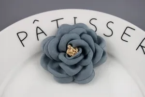 Close-up of a dusty blue fabric camellia flower brooch with yellow stamens on white porcelain