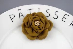 Macro shot of 6.5cm mustard yellow fabric camellia flower with petal layers on a plate