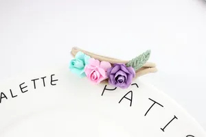 Close-up of three mini paper roses on a soft elastic nylon headband for babies