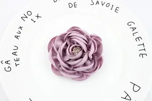 Macro view of a 7.5cm purple handmade fabric camellia with pearl center on a ceramic plate