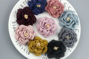 Handmade 6.5cm camellia fabric flowers in nine assorted colors on a white ceramic plate