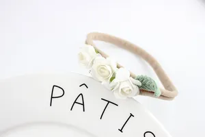 Detailed close-up of white fabric roses and green leaf on a stretch nylon baby headband