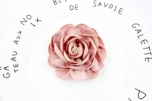 Close-up of pink handmade satin camellia flower with detailed stamens in white ceramic dish