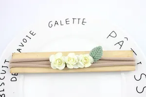 Elastic baby headband with three cream paper roses and green leaf on wooden prop