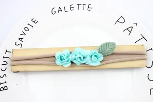 Elastic baby headband with three turquoise paper roses and green leaves on wood