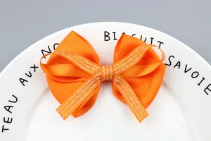 Orange grosgrain ribbon hair bow with white script lettering on a ceramic plate background