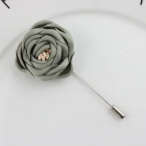 Macro view of handmade grey fabric camellia lapel pin with beads on a long metal needle