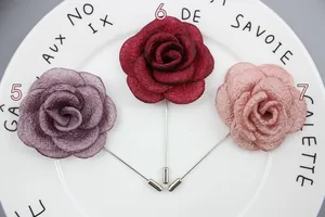 Three elegant fabric rose brooches in dusty purple, deep red, and soft pink on a ceramic tray