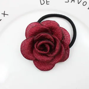 Detailansicht eines dunkelroten Stoff-Rosen-Haargummis auf einem weißen Keramikteller