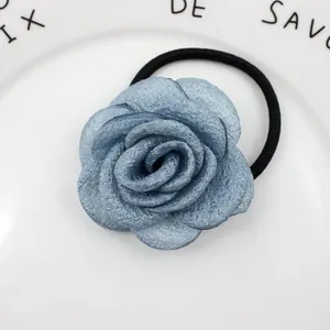 Detailansicht eines blauen Stoffrosen-Haargummis auf einem eleganten weißen Keramiktablett