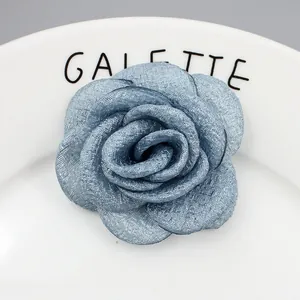 Franse grijsblauwe stoffen camelia broche met gelaagde bloemblaadjes op een wit bord