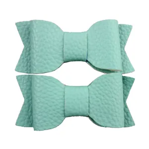 Detail view of two mint green faux leather bow hair clips with soft lychee texture