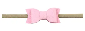 Detailed close-up of pink faux leather bow on a soft nude nylon baby headband