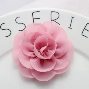 Close-up of pink handmade chiffon fabric flower with layered petals on a white ceramic plate