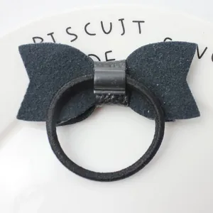 Minimalist black faux leather bow hair tie on a white ceramic plate for girls