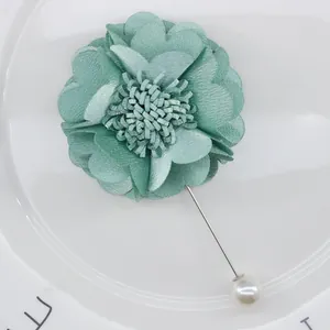 Detail of mint green fabric flower brooch with silver pin and white pearl on white plate