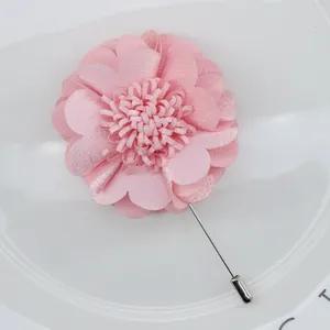 Macro shot of pink handmade fabric flower brooch with long silver needle on ceramic plate