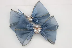 Dettaglio di fiocchi in organza blu con ricami dorati, perle bianche e strass brillanti