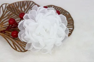 Detail of a white organza flower brooch with glittery edges on a golden ginkgo leaf tray