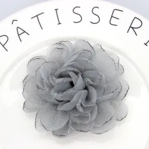 Detail of multi-layered grey organza peony hair clip with delicate burnt edges on ceramic