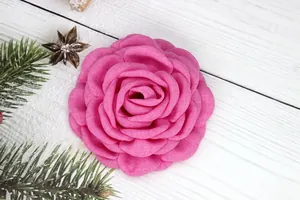 Detailed view of pink fabric rose handmade with textured petals on a rustic wood surface