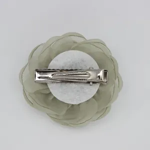 Detalle de la pinza de pelo camelia en organza verde con clip de metal plateado detrás