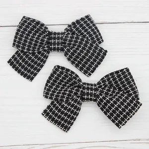 Detailed top view of a pair of black and white plaid tweed bow hair clips on wood surface