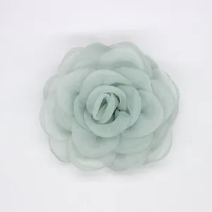 Detalle macro del broche de camelia en organza verde claro con pétalos ondulados en capas