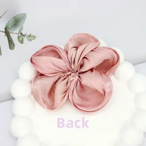 Vue détaillée du dos d'une pince à cheveux fleur en satin rose sur un plat blanc