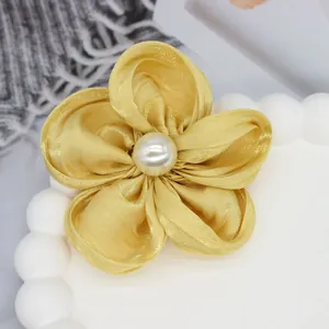 Gros plan d'une fleur en satin doré à cinq pétales avec un centre en perle polie