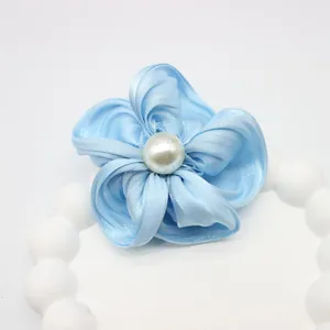 Détail d'une pince à cheveux fleur en soie bleu clair avec une perle blanche centrale