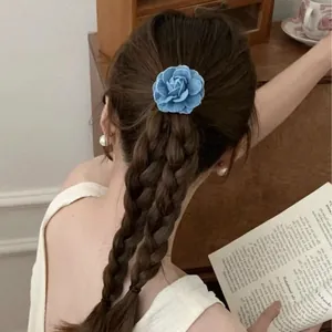 Detailed view of blue denim camellia flower hair tie worn on a braided hairstyle