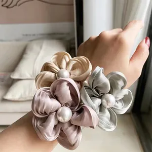 Detailed shot of three satin flower hair ties with pearls worn on a wrist as bracelets