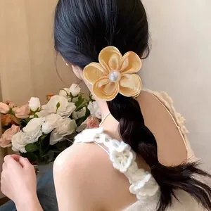 Elegant champagne silk flower hair tie with a central pearl on a braided ponytail