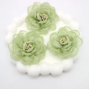 Macro detail of three 3D green organza fabric camellia flowers with bead centers