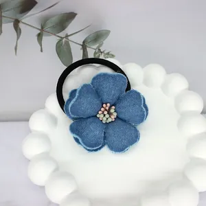 Close-up of blue denim camellia flower hair tie with beaded center on a white tray
