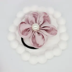 Detail of pink satin flower hair tie with a central pearl and black elastic band