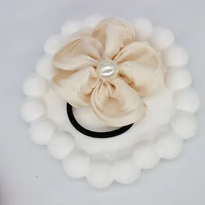 Detailed macro view of champagne satin flower hair tie with central white pearl accent