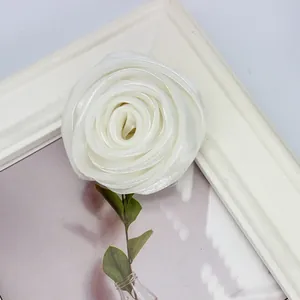 Detailansicht der weißen Satin-Rosenknospe mit grünen Blättern auf Deko-Hintergrund