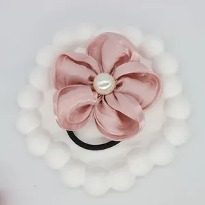 Detailed view of dusty rose satin flower hair tie with central faux pearl on white tray