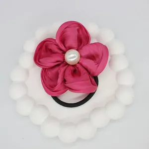 Close-up of a pink satin flower hair tie with a white pearl on a decorative plate