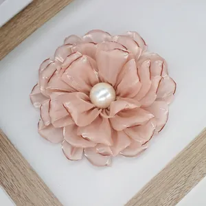 Detail of a peach silk peony brooch with a central pearl on a white background