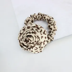 Detail of leopard print hair scrunchie featuring a 3D fabric rose on white marble
