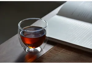 Dettaglio di un bicchiere a doppia parete resistente al calore con tè rosso su legno