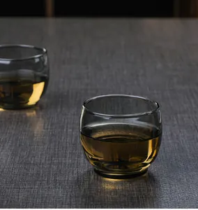 Close-up of heat-resistant grey glass tea cup with golden tea on dark textured surface