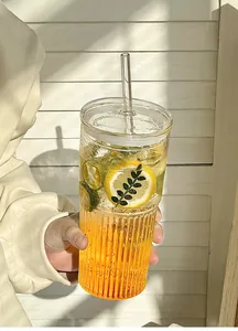 Close-up of hand holding a ribbed glass cup with lid, straw, and refreshing cold drink