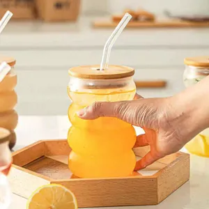 Minimalist ripple glass cup with bamboo lid and straw held in hand over a wooden tray