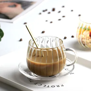 Nahaufnahme einer gestreiften Glas-Kaffeetasse mit Untertasse und goldenem Löffel