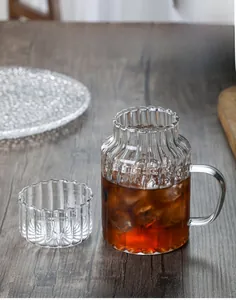 Detail of ribbed glass tea set with large handle and multi-use lid on wooden surface