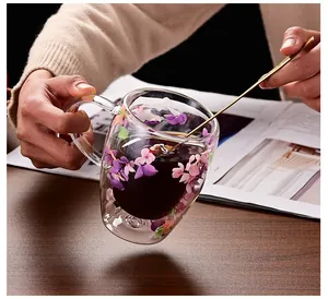 Detail von doppelwandigem Glasbecher mit Trockenblumen und Goldlöffel auf Holztisch